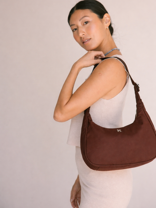 Woman carrying a brown handbag against a plain background with metal logo color is chestnut
