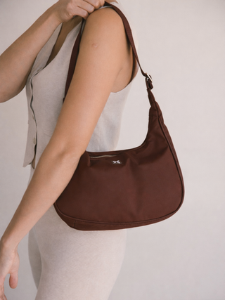 Brown hobo shoulder bag purse style in chestnut being carried by a person on a plain background
